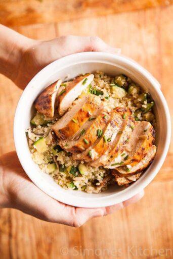 Person holding a quinoa bowl with spicy harissa chicken