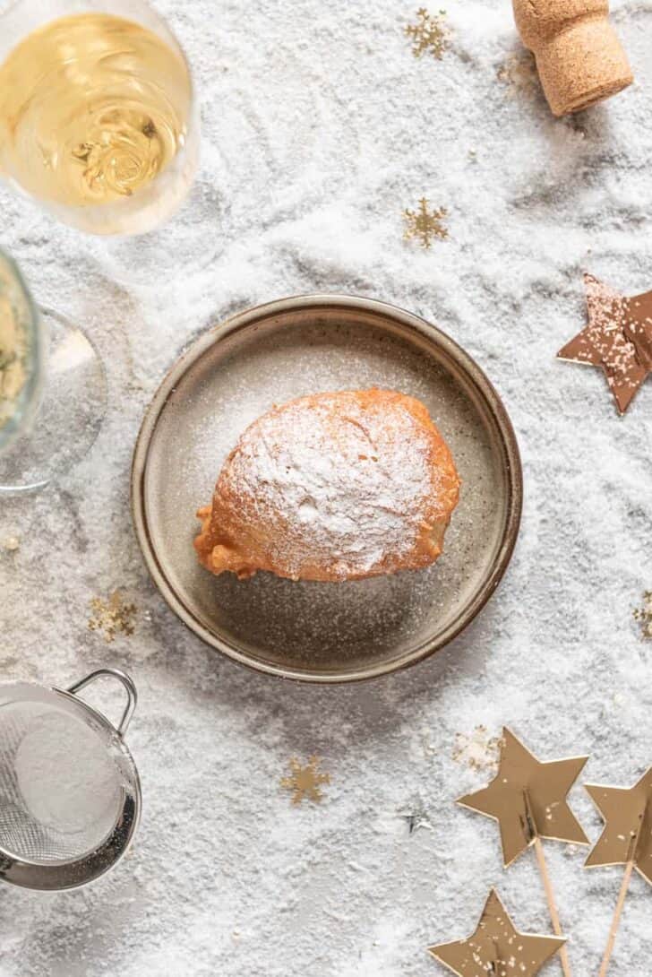 One single doughnut on a small plate with icing sugar