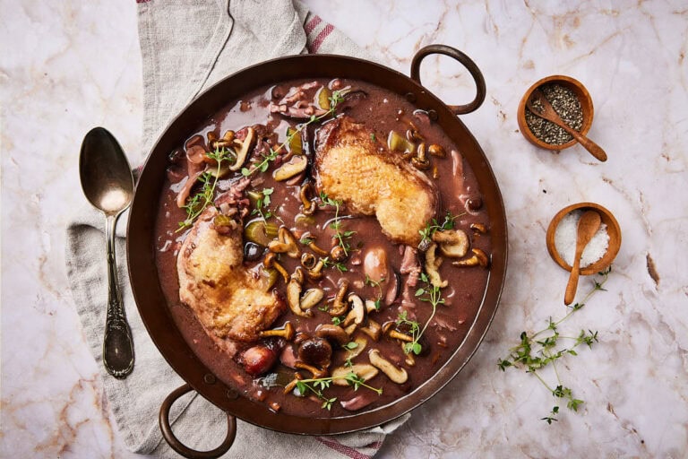 Easy coq au vin recipe in a pan with herbs and a spoon