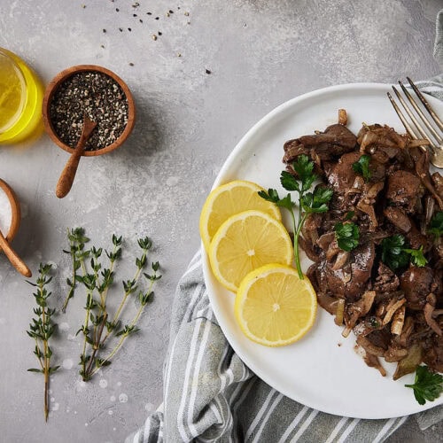 Plate with prepared chicken liver on a grey background with herbs