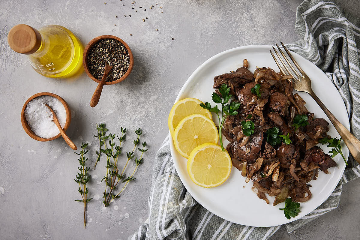 Plate with prepared chicken liver on a grey background with herbs