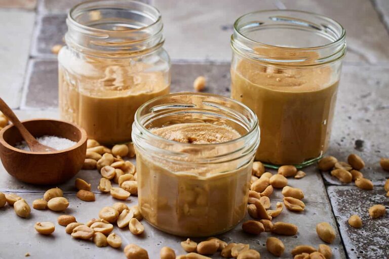 Peanut butter recipe in three jars with some peanuts around it