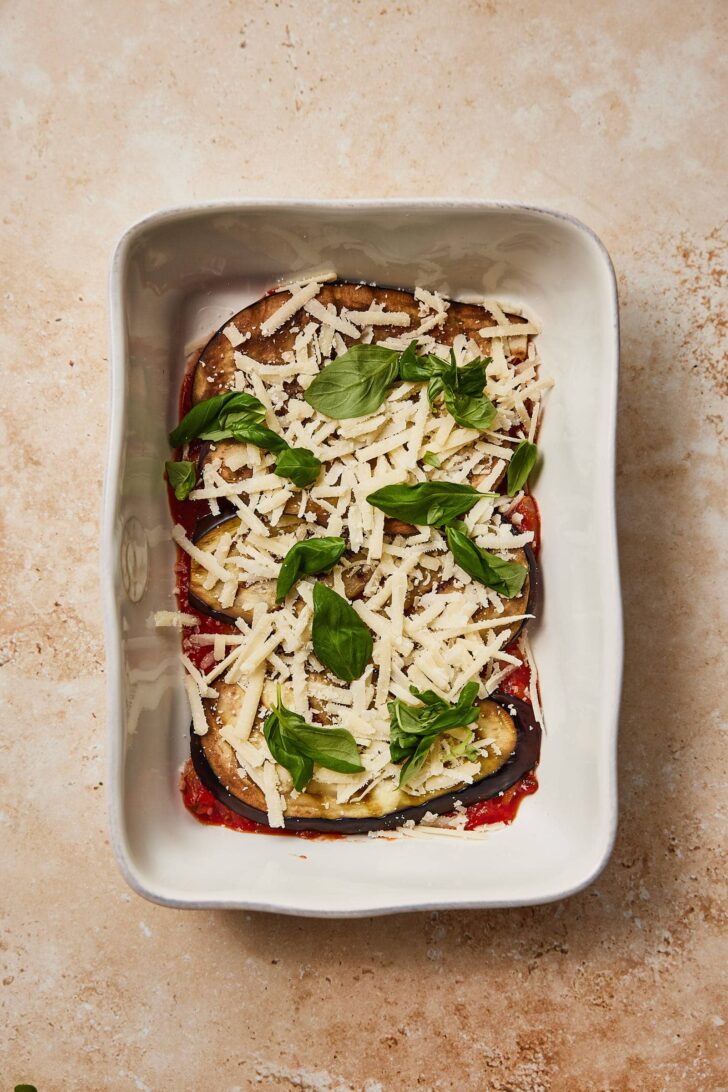 Adding a generous layer of granted cheese on top of the eggplant slices 