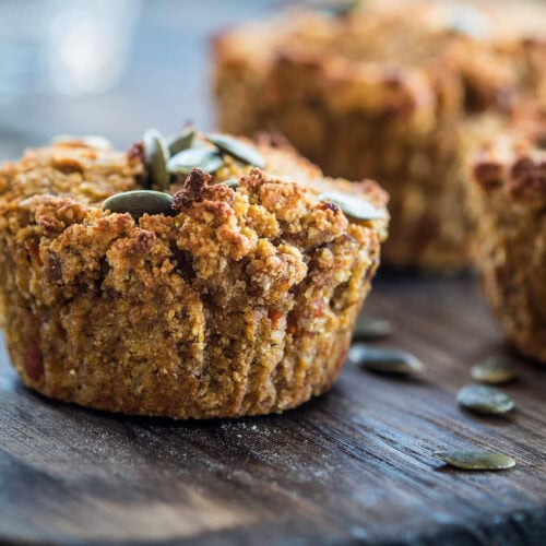 Close-up of vegan pumpkin muffins topped with pumpkin seeds on a wooden surface.