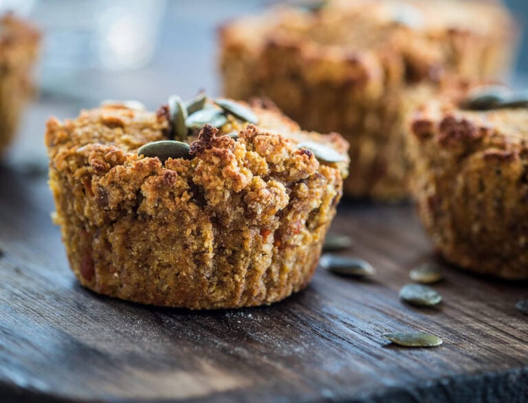 Close-up of vegan pumpkin muffins topped with pumpkin seeds on a wooden surface.